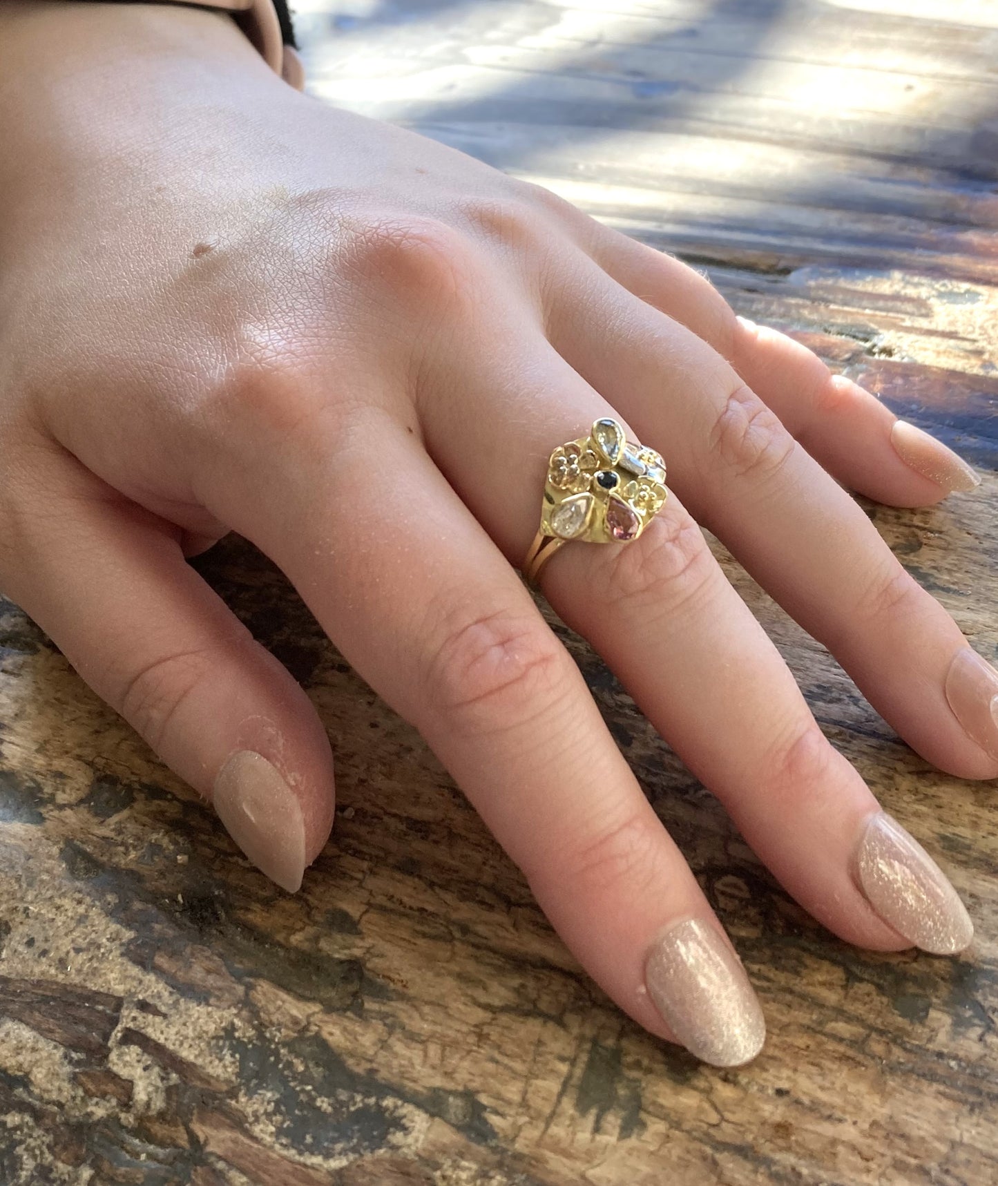 yellow gold and sapphire floral ring on ladies hand, wood background
