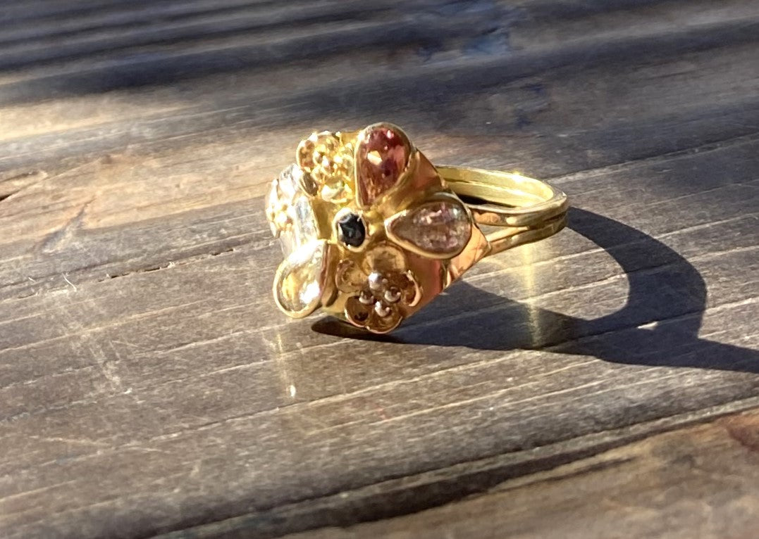 rich 18ct yellow gold floral cocktail ring set with pink, white, blue and green sapphires, on wood background