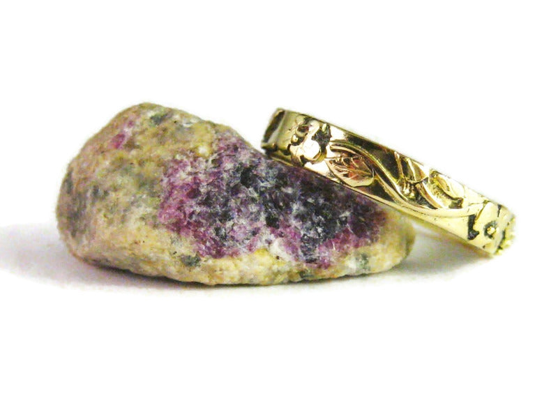 pretty handmade 18ct gold unisex wedding ring with floral raised details, resting on a purple stone, on white background