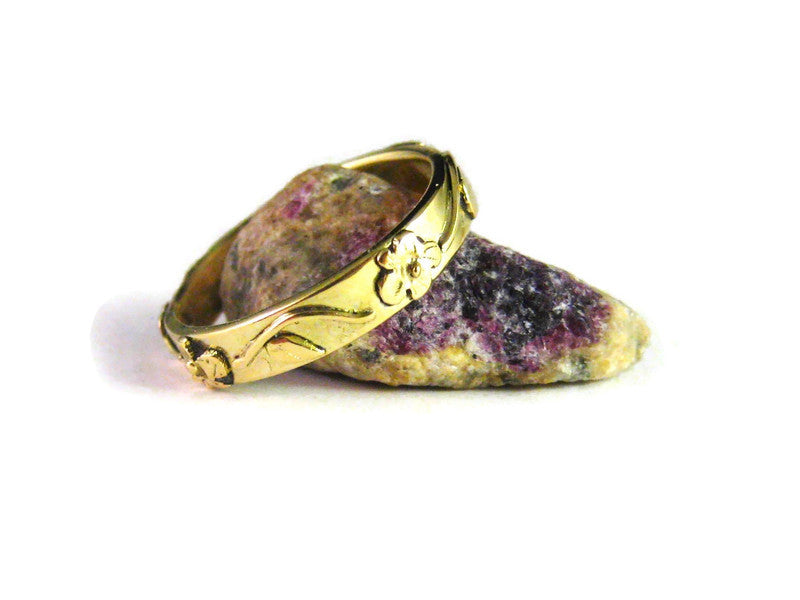 18ct yellow gold floral garden wedding ring with flowers and leaves in relief around the band, resting against an amethyst crystal, on white backf=ground