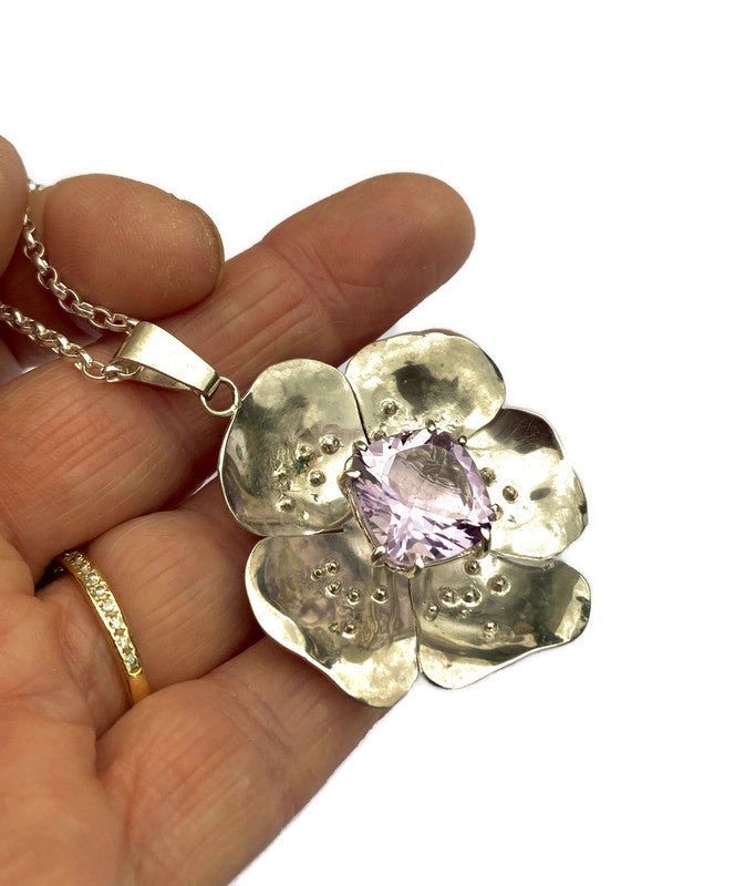 Large silver flower pendant with square purple amethyst in the center, held on hand