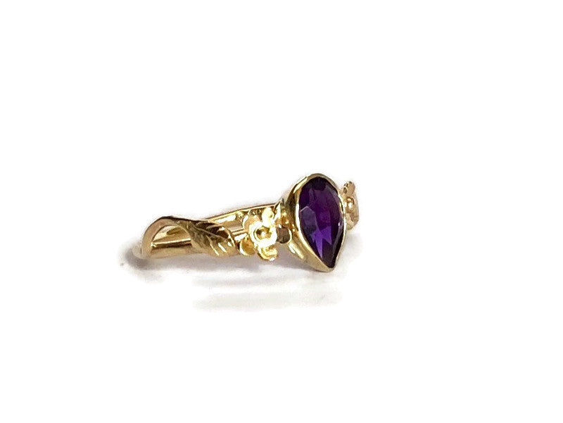 artisan gold ring set with pear shape dark amethyst, with leaves and flowers, on white background