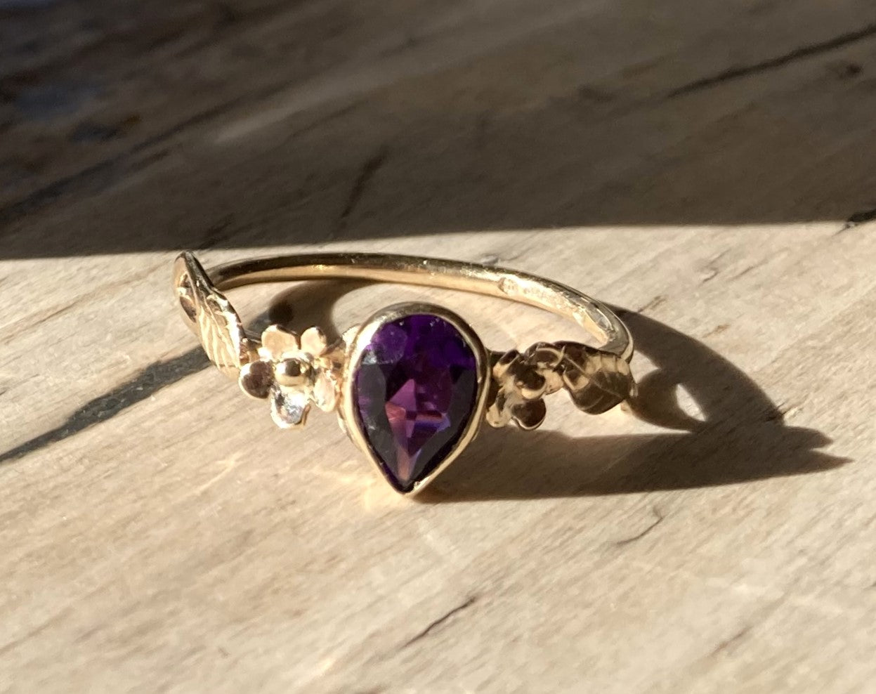 gold floral ring with large pear shape amethyst, on wood grain background