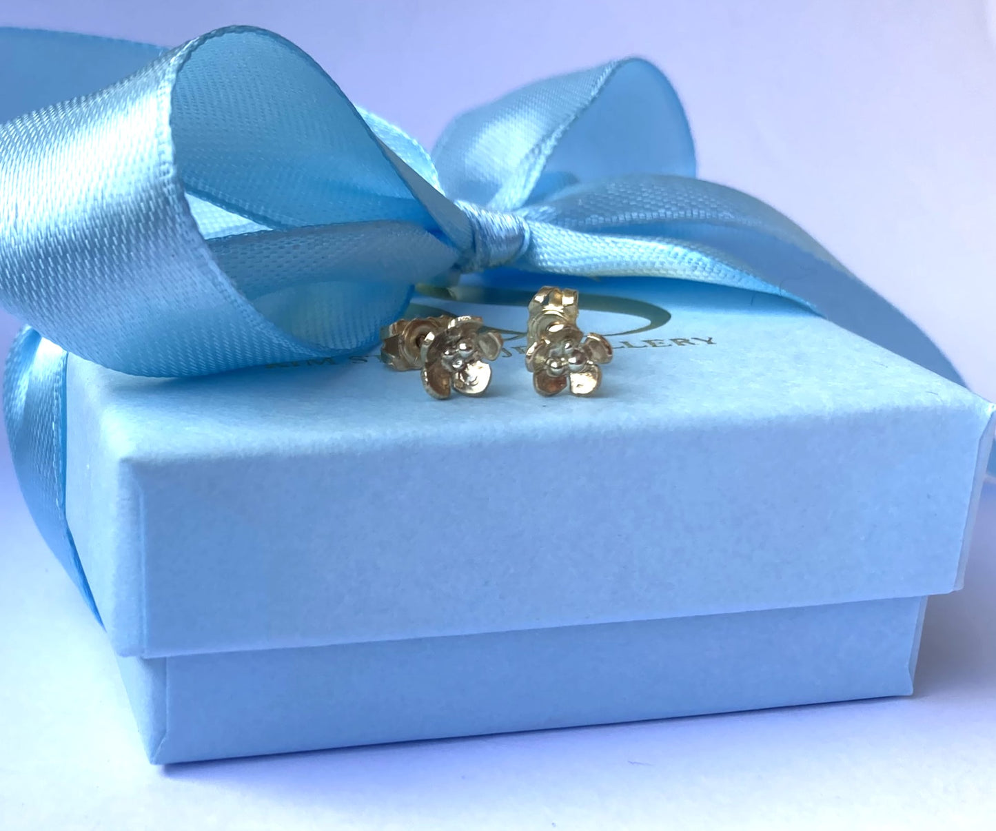 Small gold flower stud earrings on pale blue box with blue ribbon bow