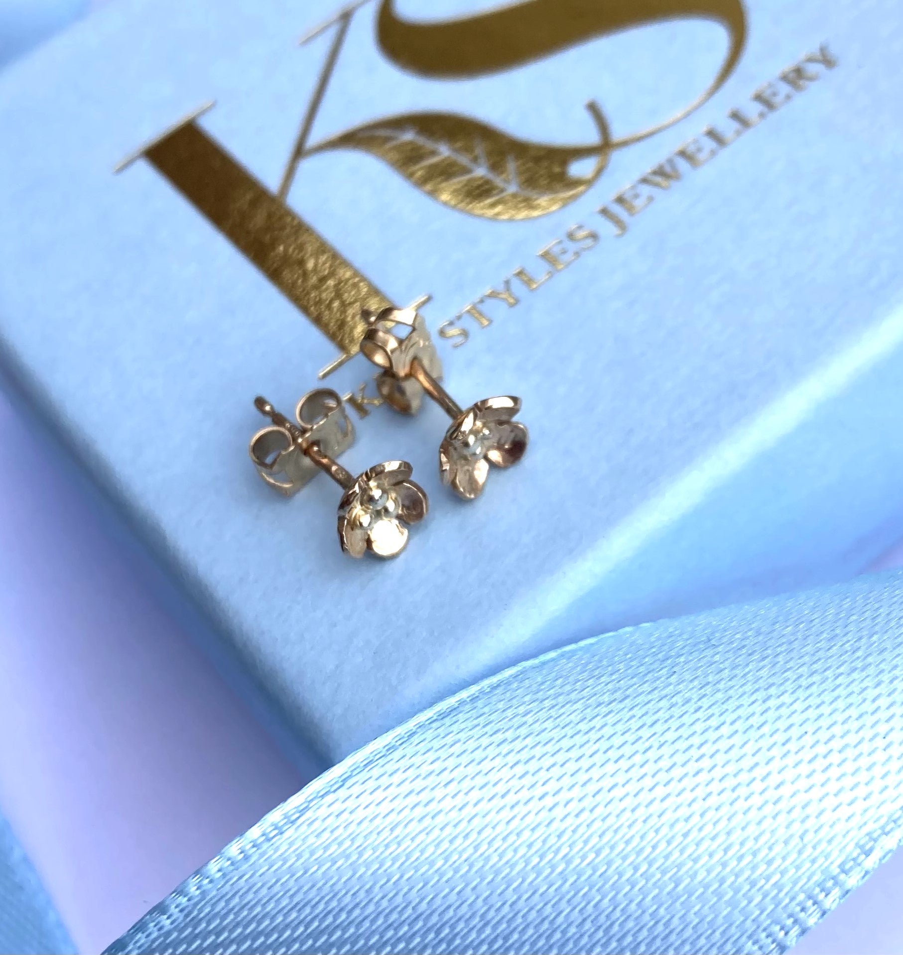 small gold floral stud earrings on pale blue gift box