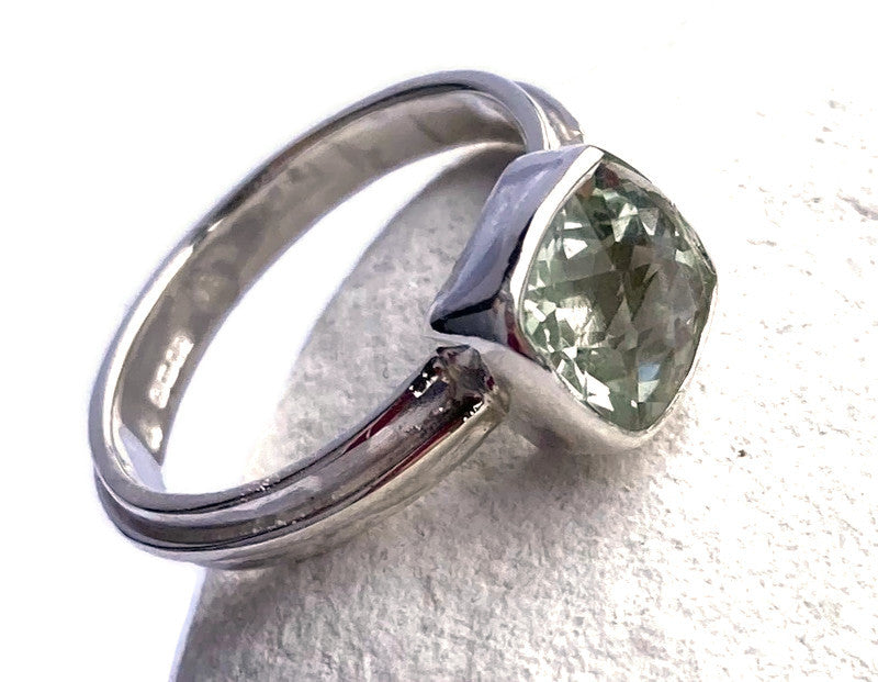 silver ring set with square green gemstone, on white pebble