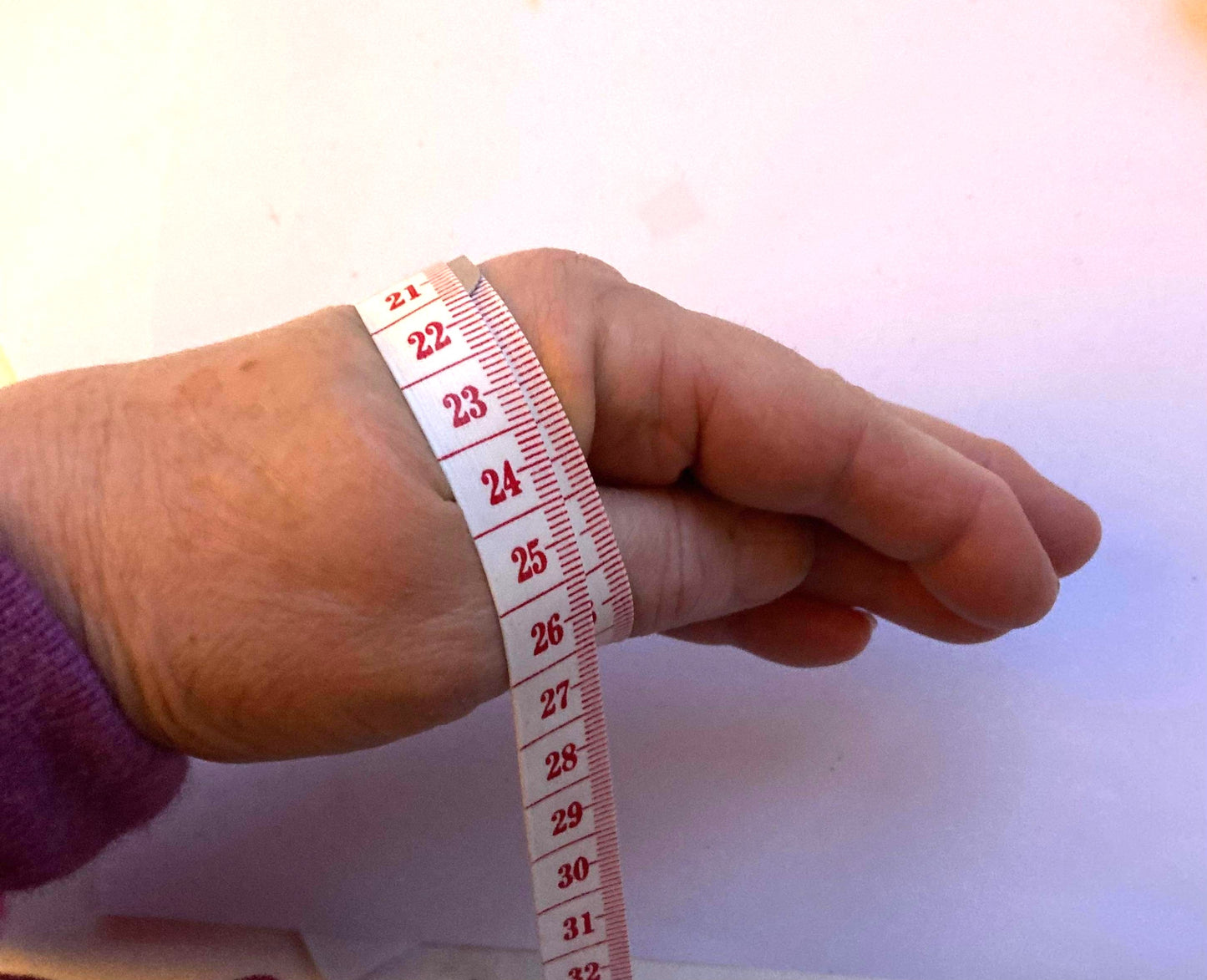 Hand with tape measure wrapped around it for measuring bangle size, on white background