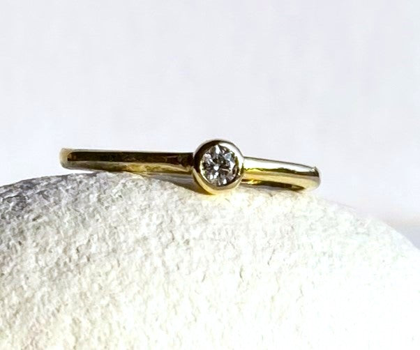 dainty engagement ring in 18ct yellow gold with round diamond, on white pebble