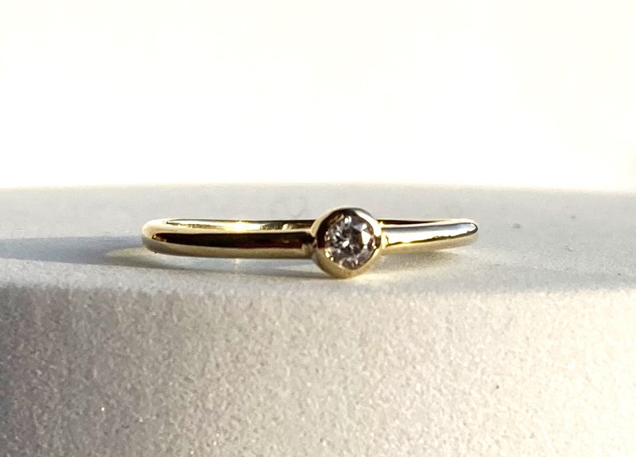 18ct yellow gold simple engagement ring with round diamond on grey background