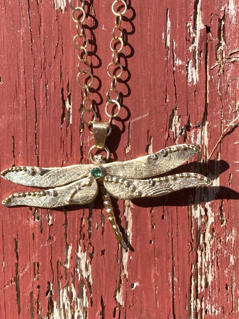 Gold Dragonfly-shaped pendant necklace on a red wooden background