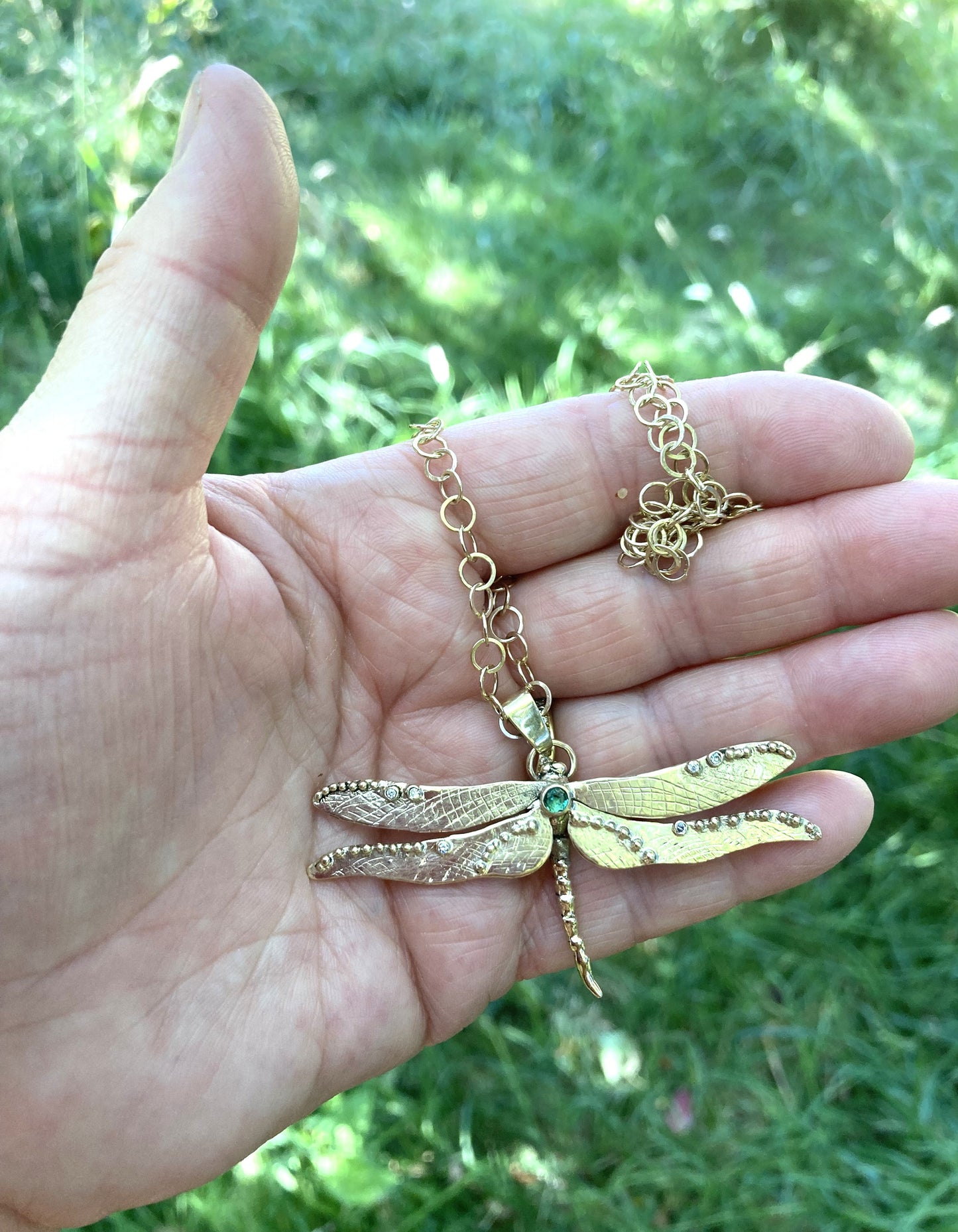Gold dragonfly necklace held in a hand with a grassy background