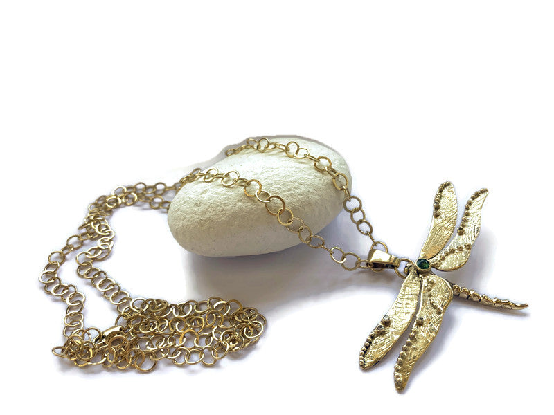Kim Styles gold dragonfly pendant on long handmade gold chain, resting on white pebble on white background