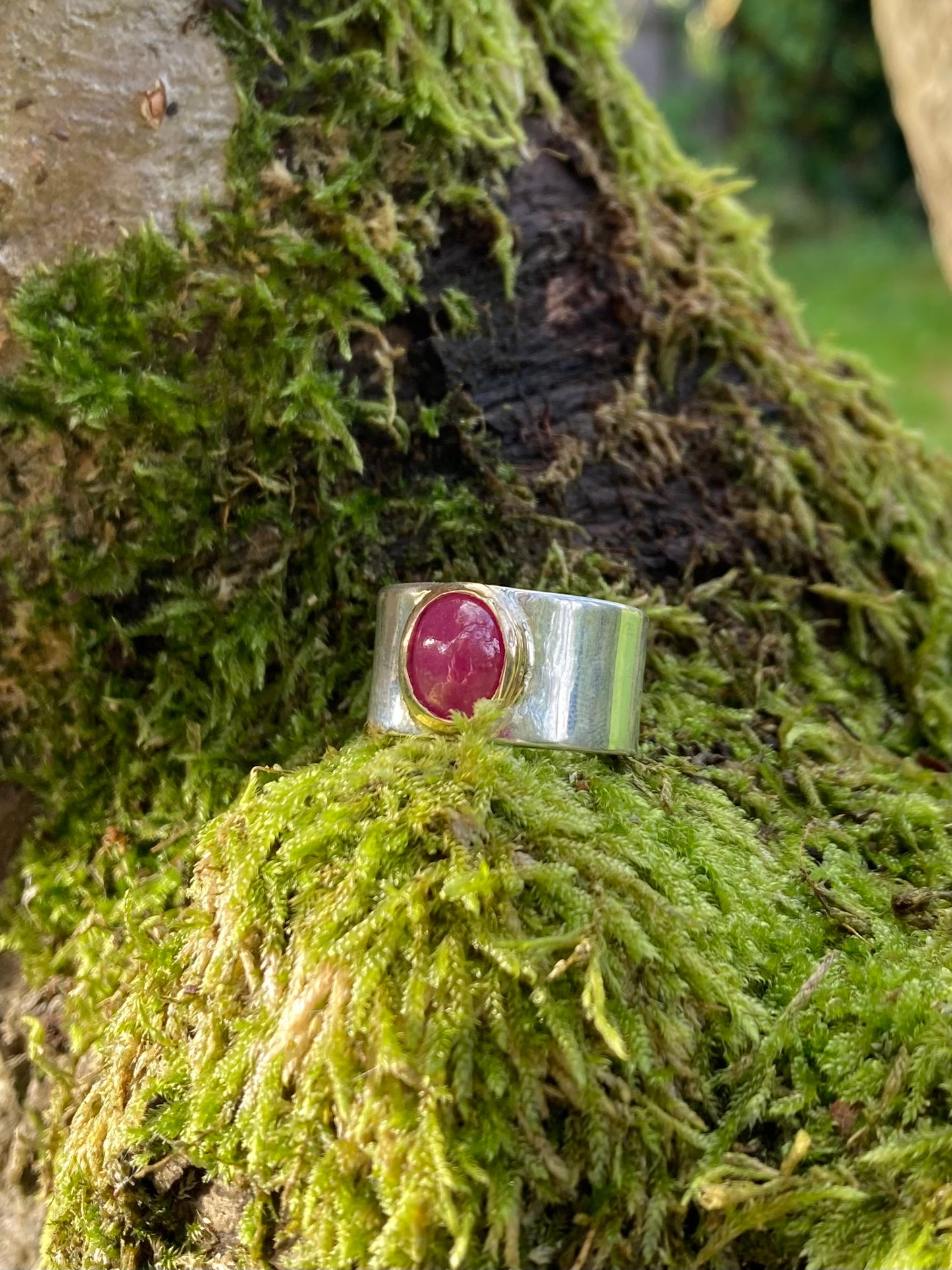  wide silver ring with large oval cabochon red ruby set in yellow gold, resting on moss