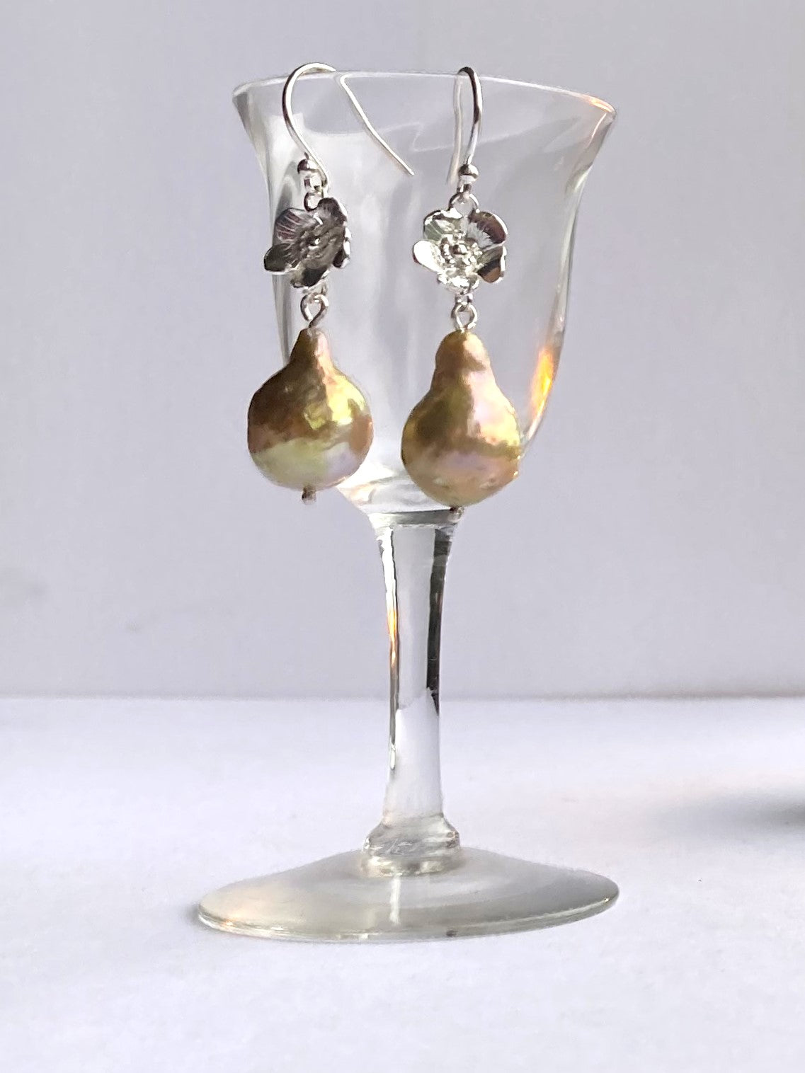 golden baroque pearl floral drop earrings, hanging on small glass
