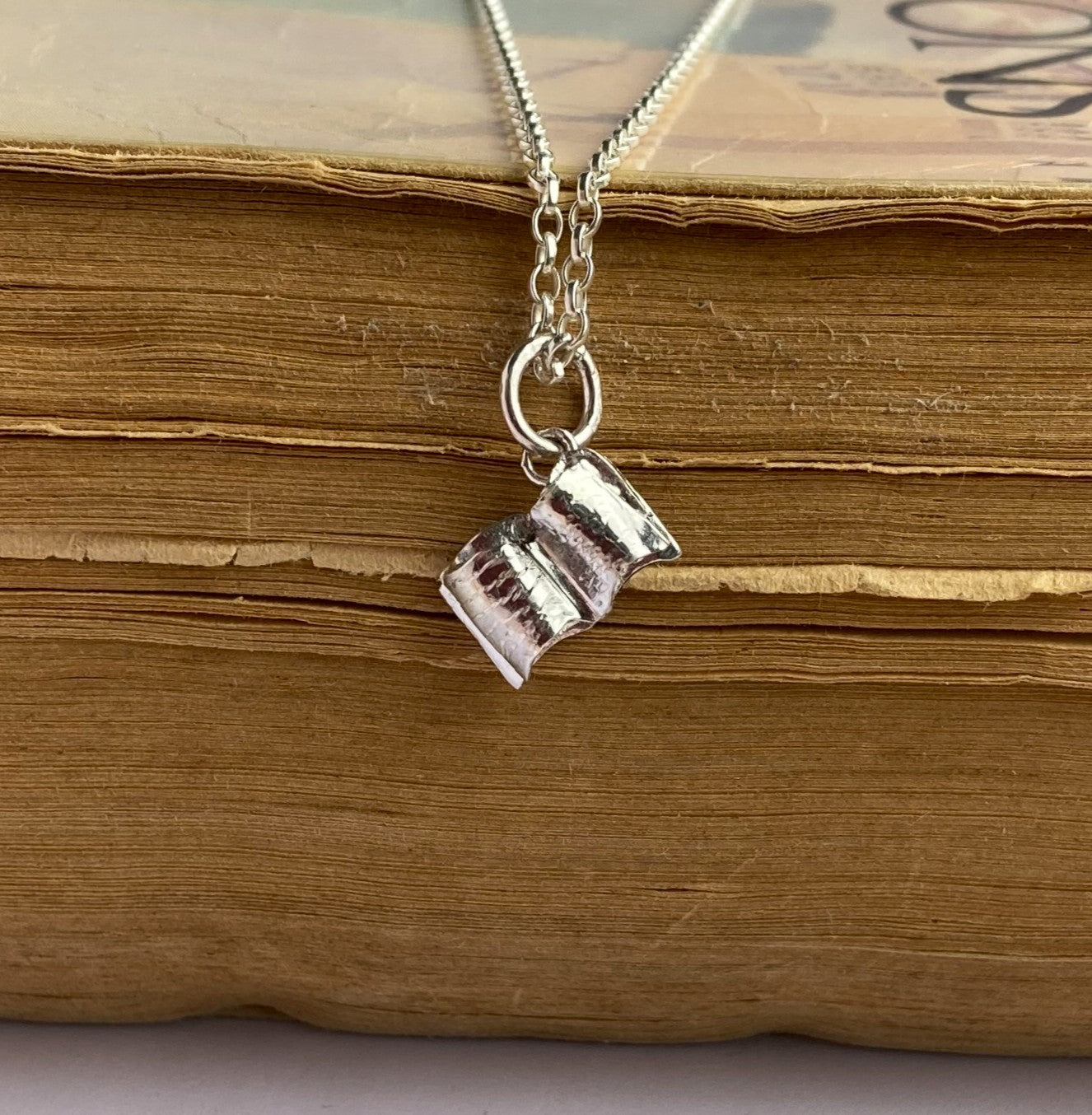 Tiny silver open book pendant on old book pages