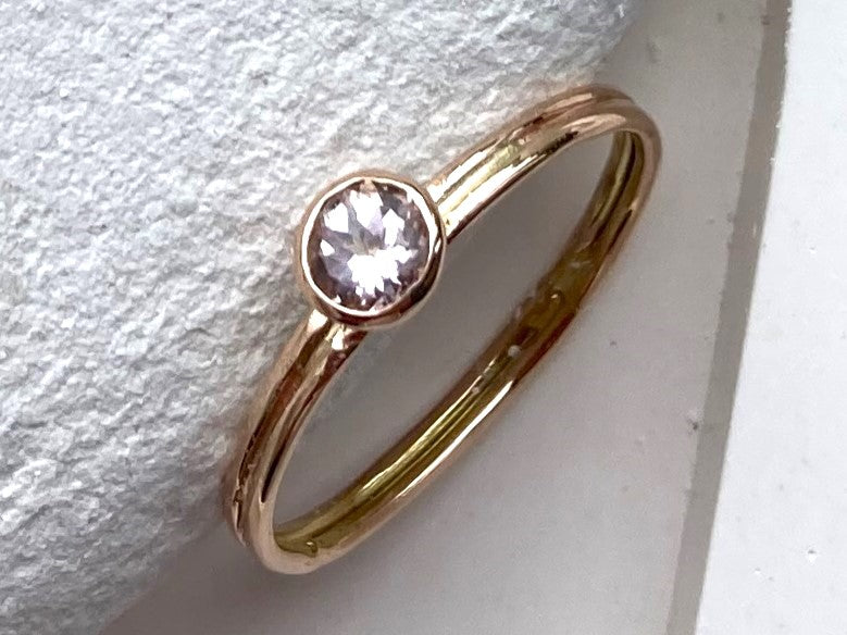 round pale pink morganite set in rose gold solitaire ring, on white stone background