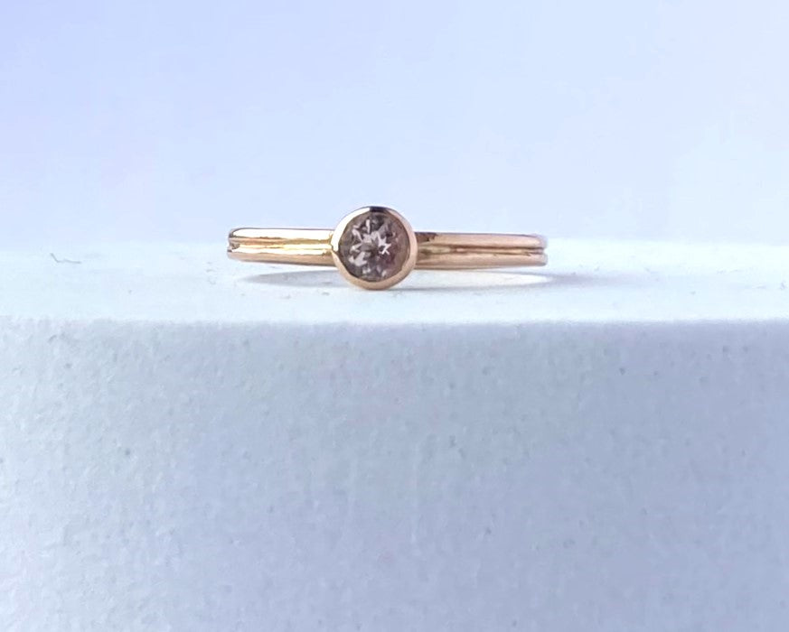 morganite and rose gold solitaire ring lying flat on grey plinth