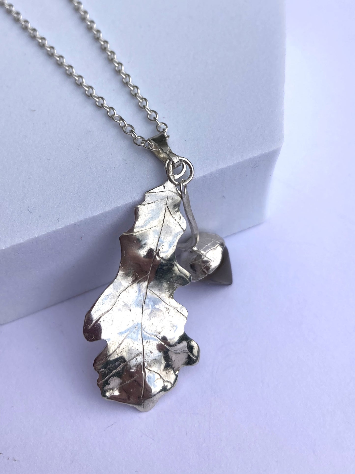 hand forged silver oak leaf with gemstone acorn, leaning on grey block