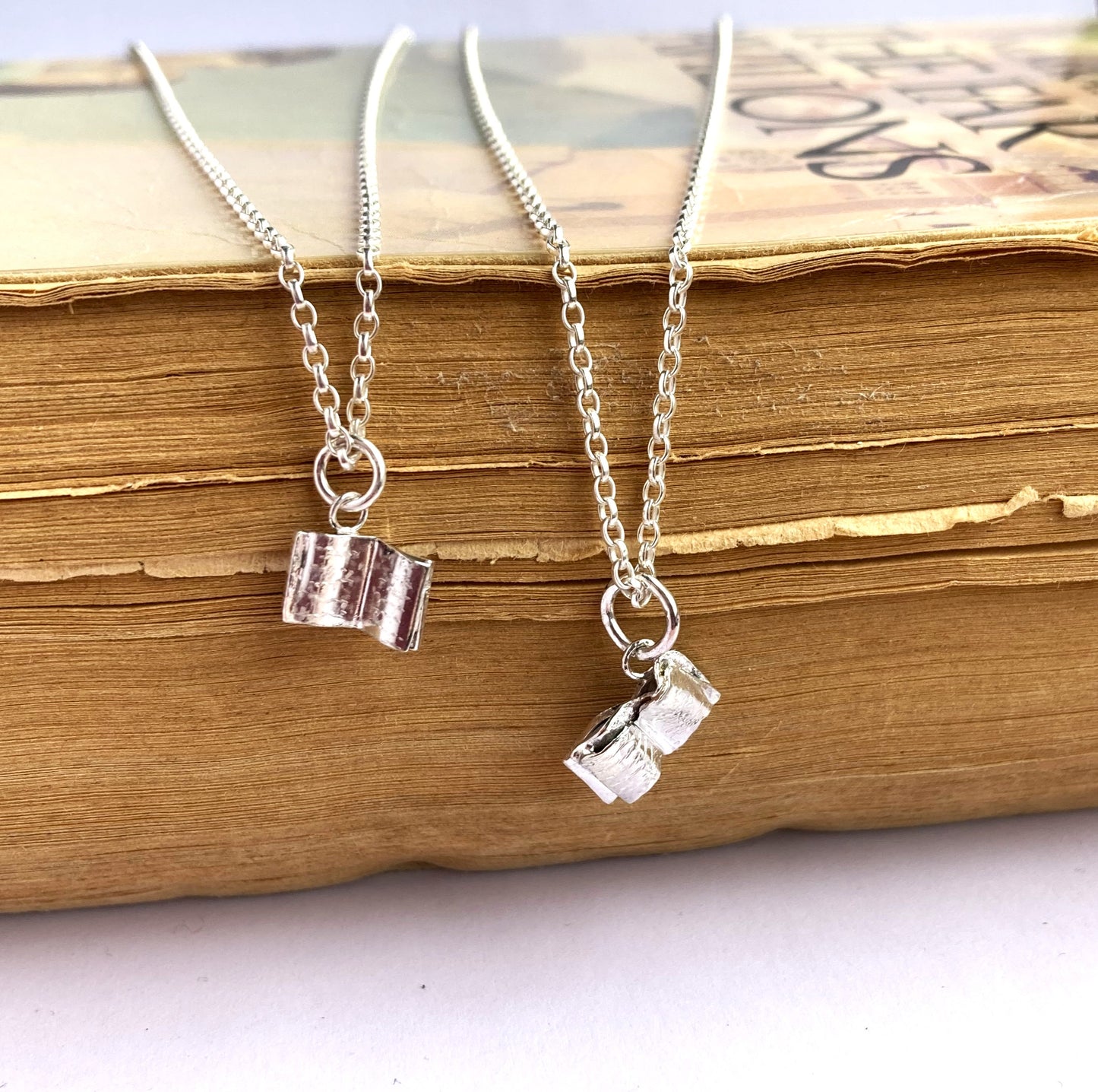 two miniature silver open book pendants, on an old book