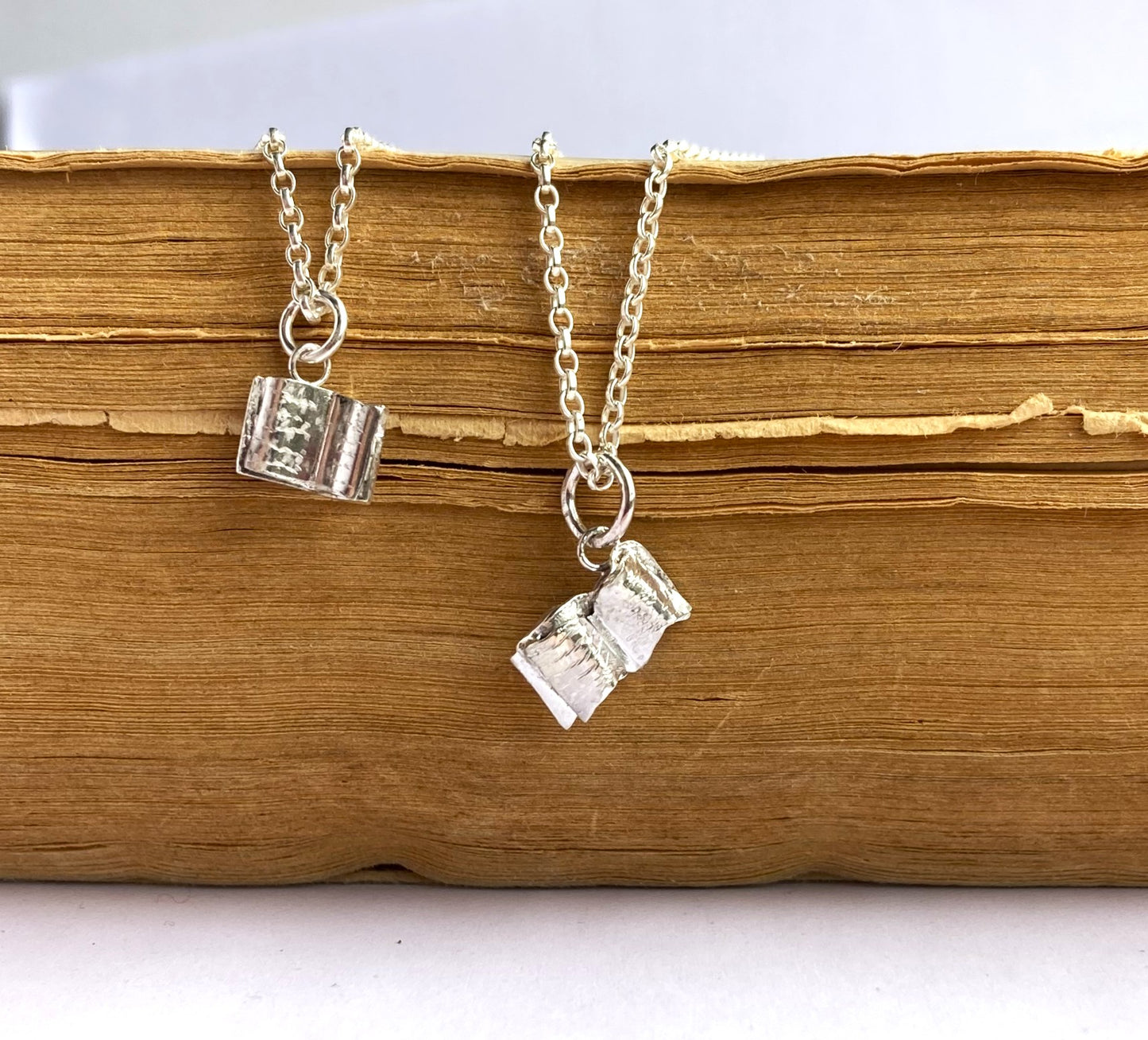 two tiny silver book pendants on an old book
