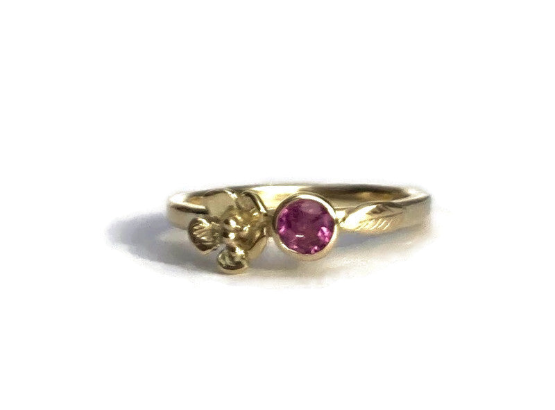 asymmetrical floral gold alternative engagement ring with round pink gemstone, on white background