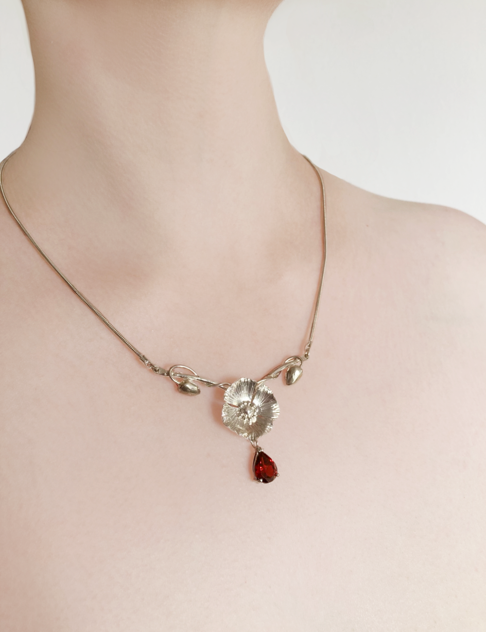 pretty floral necklace with central poppy and large garnet drop, on ladies neck