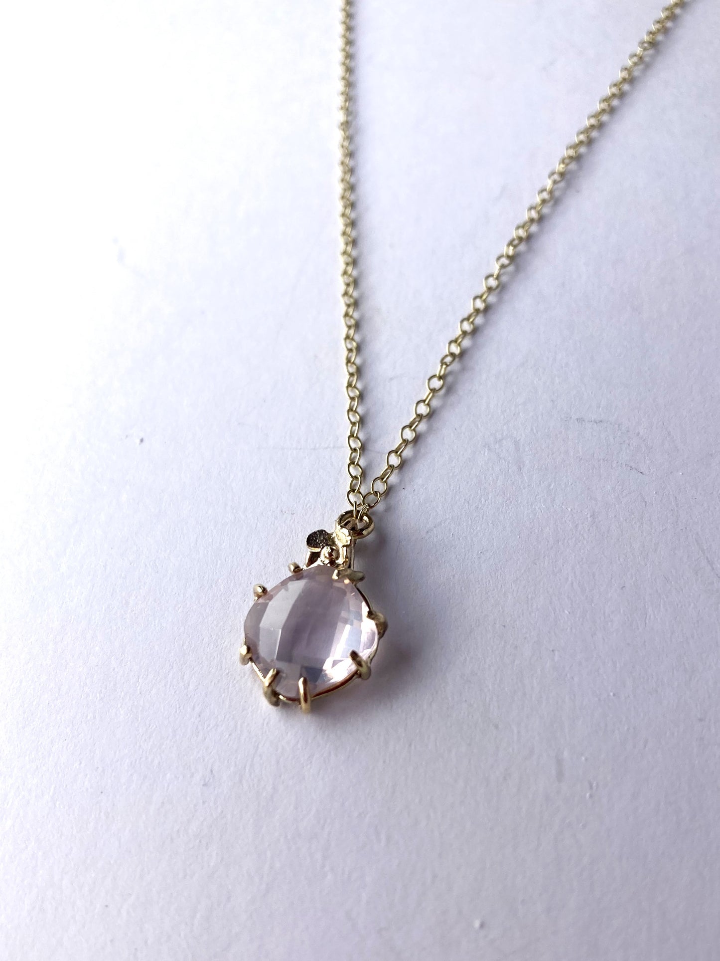 gold pendant and chain with pale pink gemstone, on grey background
