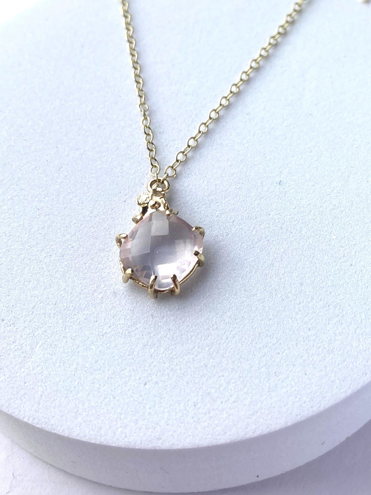 prong set pink gemstone pendant and chain, on white plinth