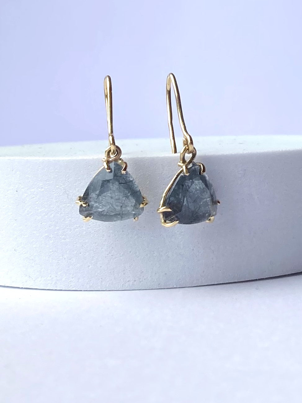 Handmade earrings with triangle grey rutilated quartz stones set in gold, on a white background