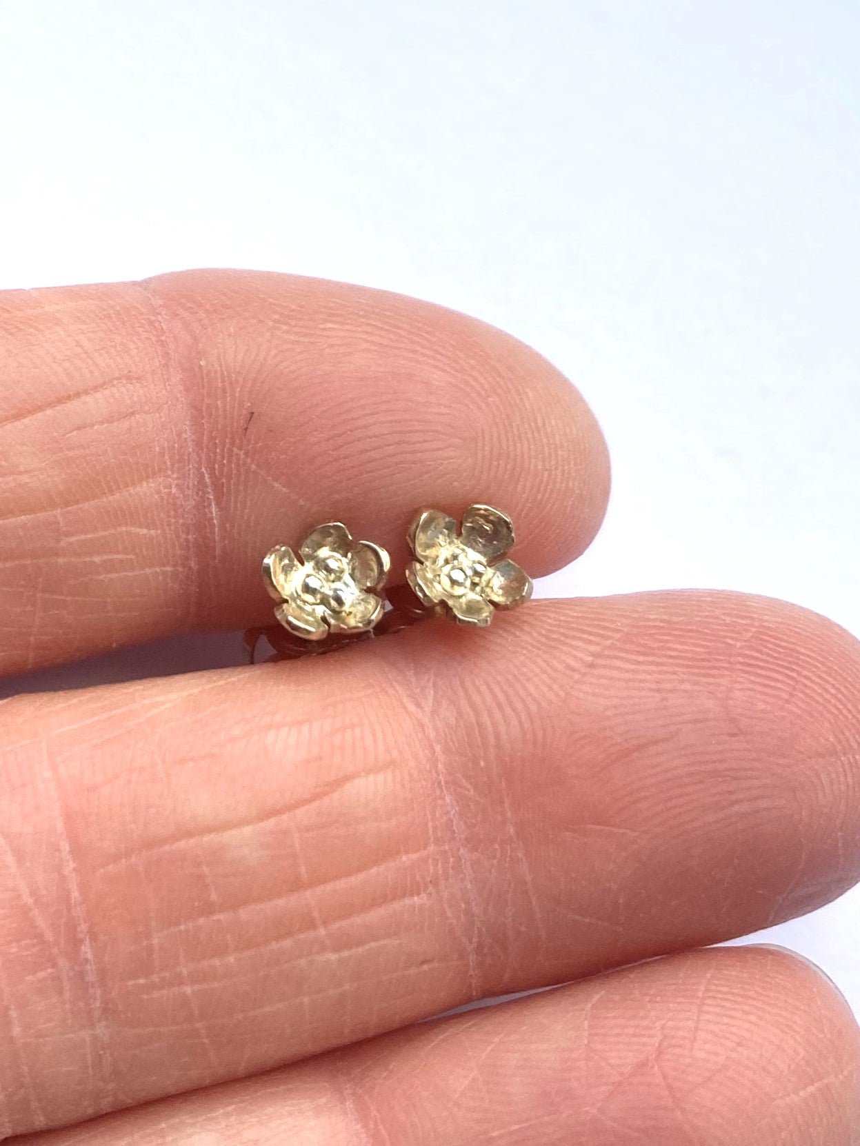 Tiny gold flower stud earrings held between two fingers