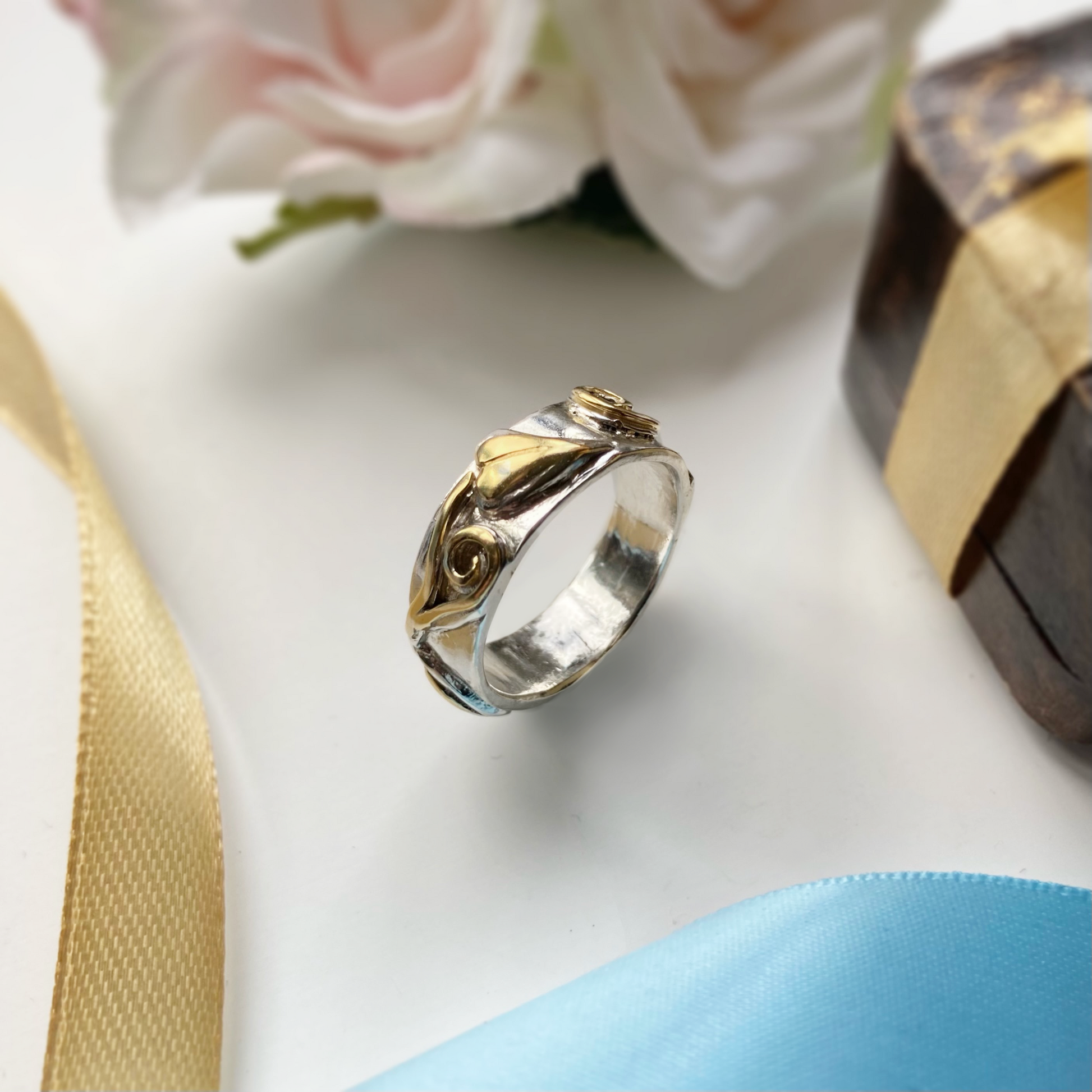 wide two colour gold ring with scroll and leaf detail, with gold ribbon and vintage box in background