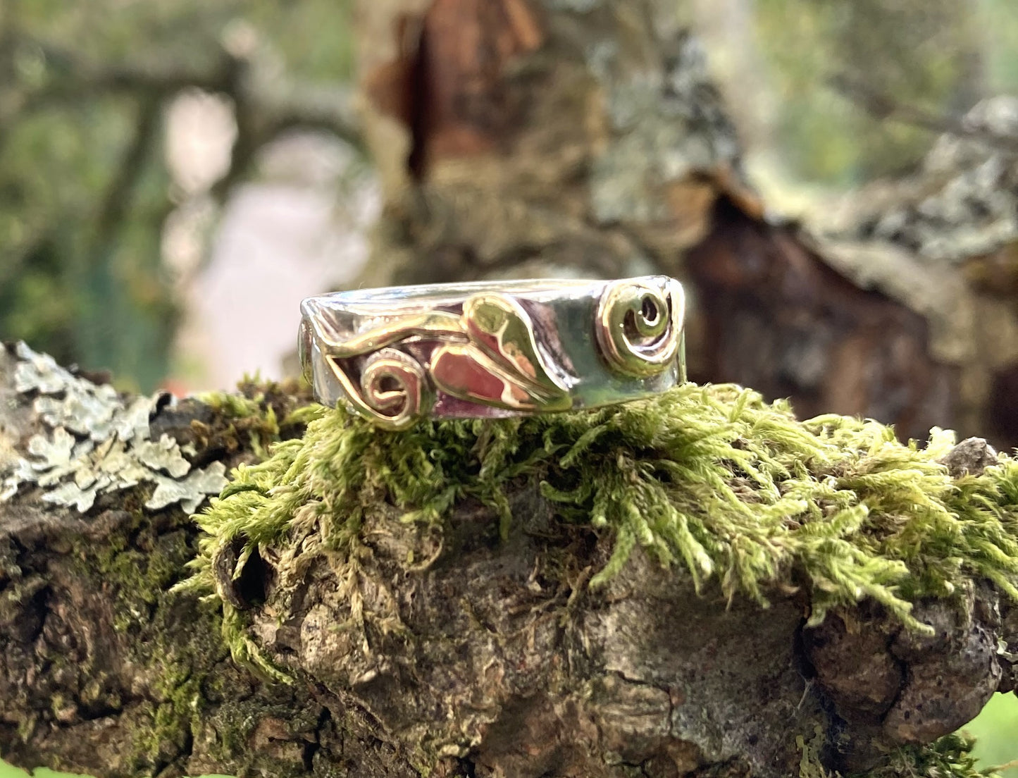 Wide wedding band in white and yellow gold with leaf detail, resting on moss