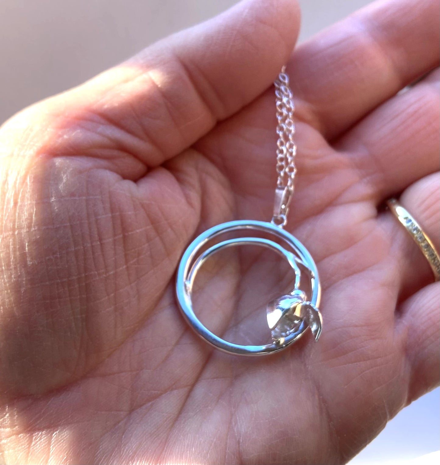 hand holding silver circle and snowdrop pendant