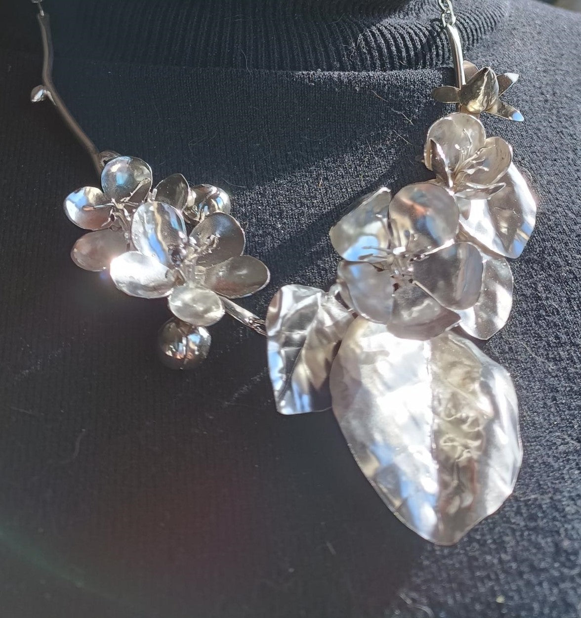close up of hand forged sterling silver botanical necklace of apple blossom and quince flowers and leaves, on black jumper