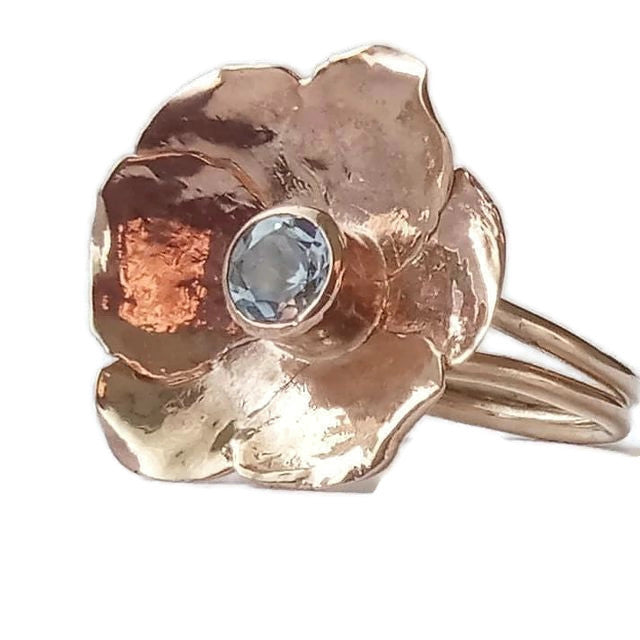 dual shank single gold flower cocktail ring set with pale blue gemstone, on white background