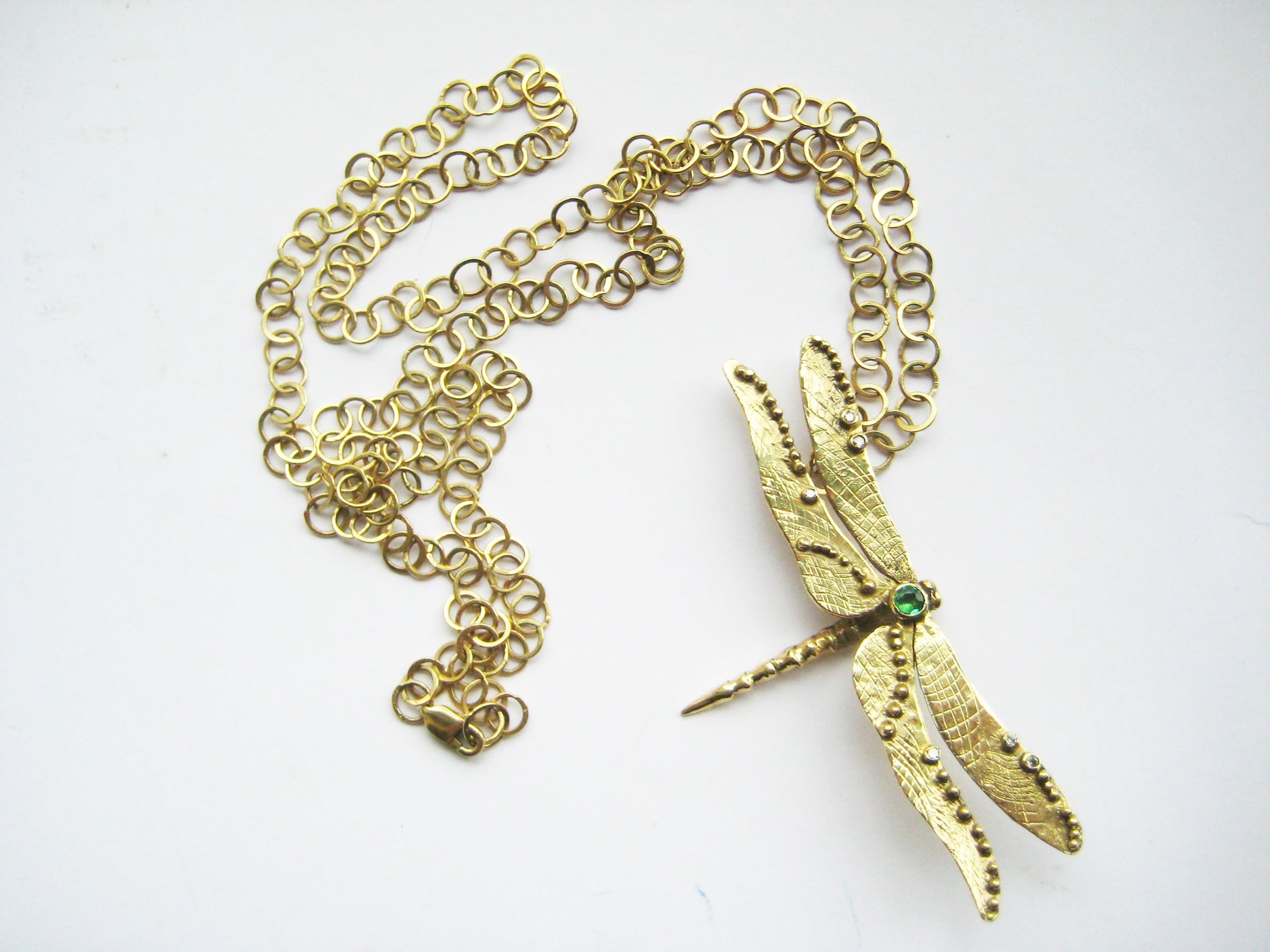large link gold chain lying loosely with yellow gold dragonfly pendant on white background