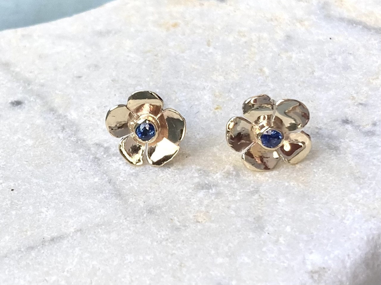 round blue sapphires in yellow gold floral setting stud earrings on marble background