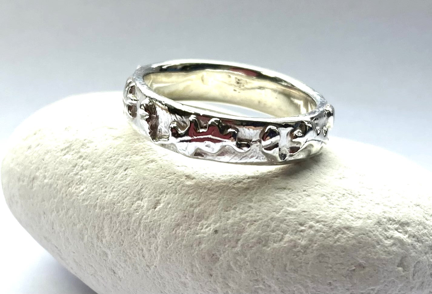 oak and acorn pattern unisex wedding ring in white metal, resting on a white pebble