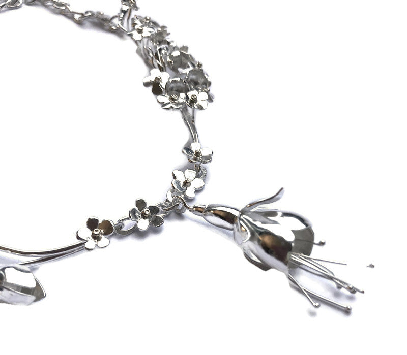 close up detail of handmade botanical necklace with silver forget-me-nots and fuchsia, on white background