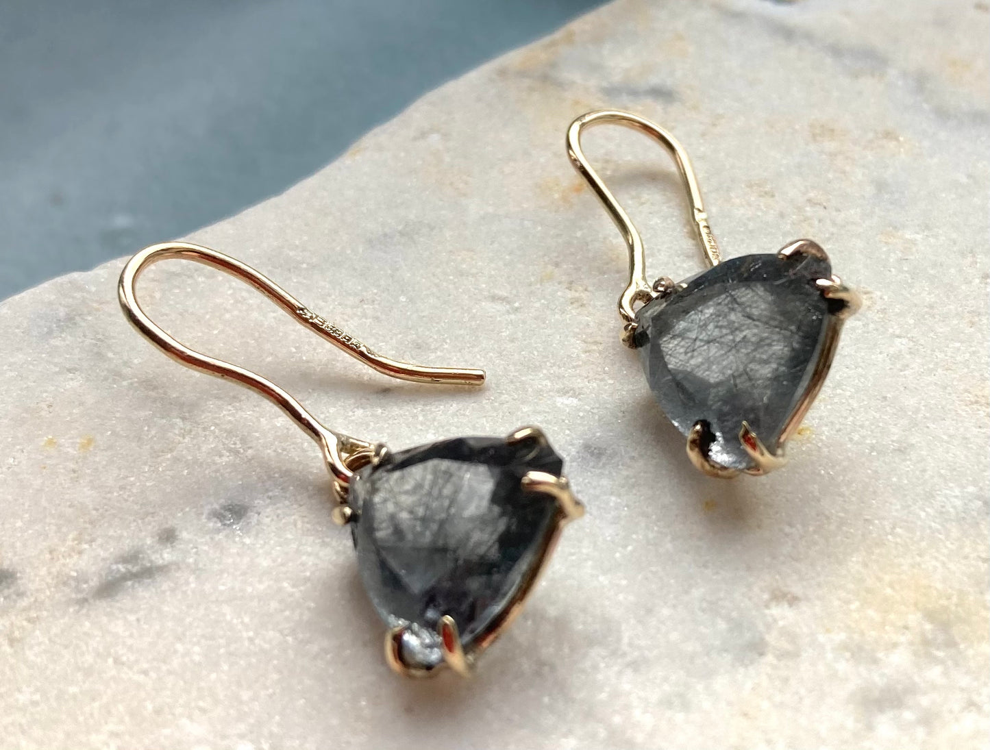 hallmarked gold prong set drop earrings with triangle rutilated quartz, on marble background