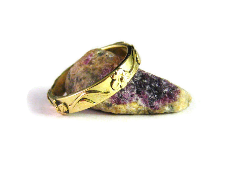 yellow gold wedding ring with flowers and leaves in relief around the band, resting on an amethyst crystal