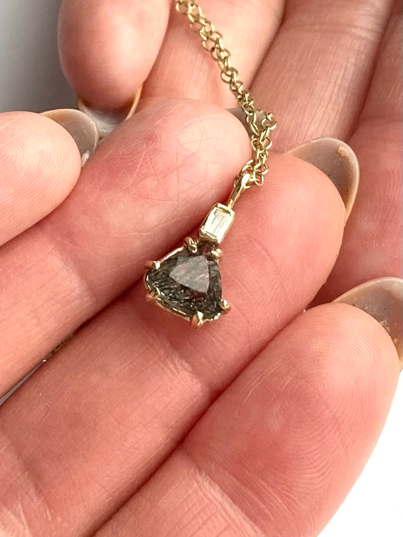 Gold rutilated quartz necklace with a trillion shape pendant held between fingers