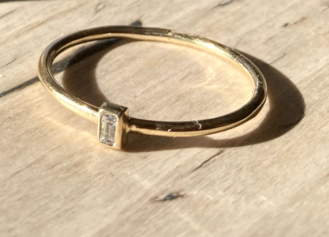 slim gold ring with baguette diamond, on wood texture