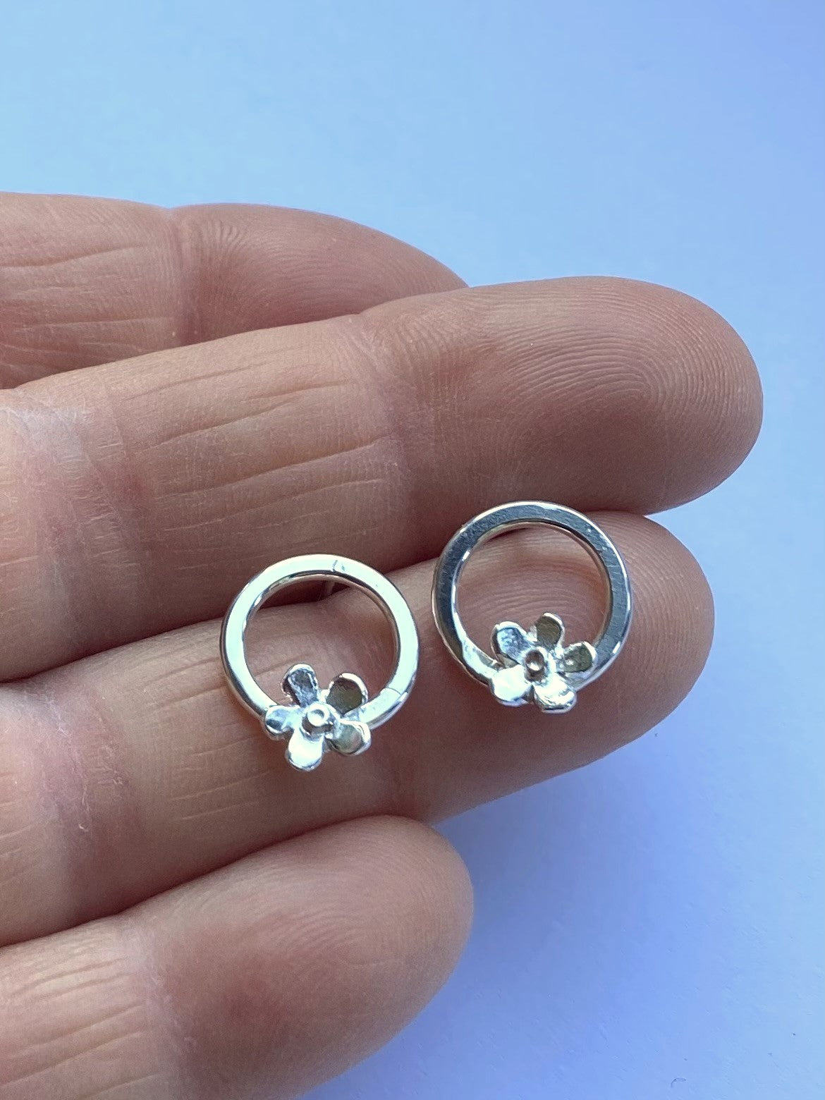 fingers holding small circle stud earring with tiny flowers