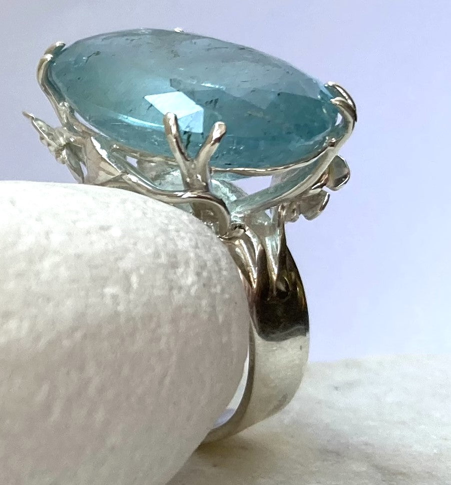 large aquamarine statement ring with floral organic setting, resting on white pebble