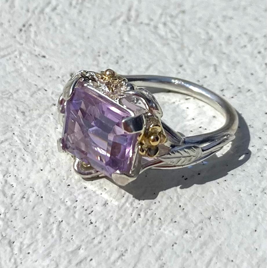 oblong amethyst with prong setting in silver and gold floral ring with gold flowers, on grey background