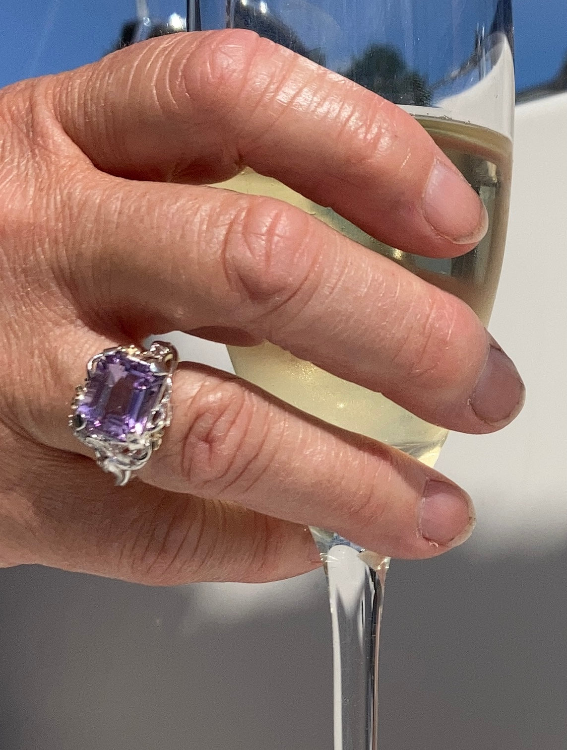 fancy oblong amethyst ring with floral details, on hand holding glass of wine