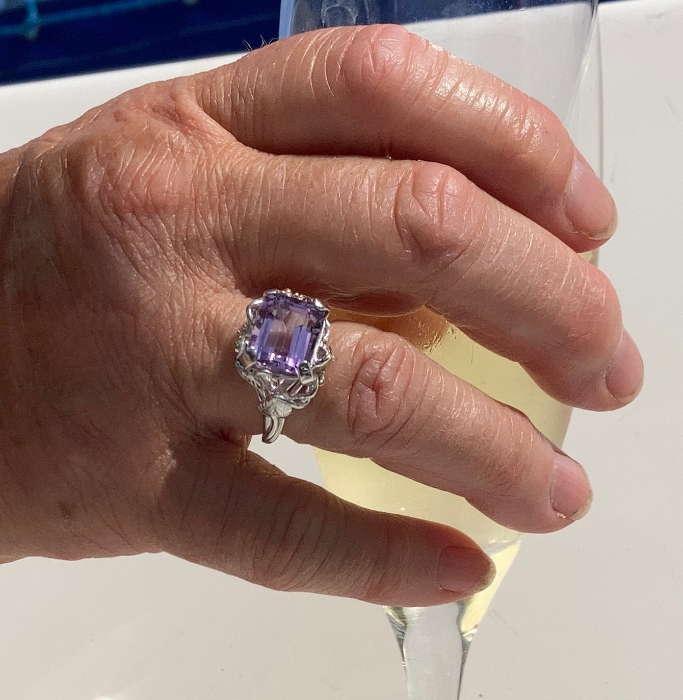 hand wearing purple gemstone cocktail ring, holding wine glass