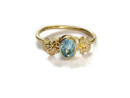 gold floral ring set with oval pale blue gemstone with flowers each side, alternative engagement ring,  on white background
