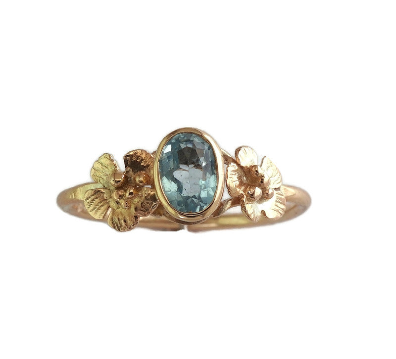 yellow gold ring with pretty flowers flanking the central oval blue topaz gemstone